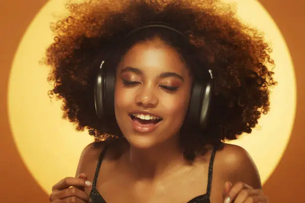Photo of African woman singing a song, wearing headphones, isolated on brown studio background