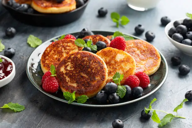 Cottage cheese pancakes served with blueberries, raspberries, strawberry jam and mint leaves, healthy vegetarian protein breakfast.