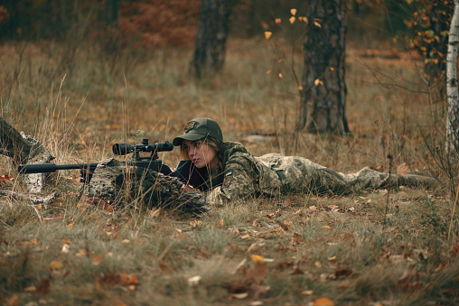 Ukrainian soldier woman dressed military uniform lying on ground with sniper rifle with silencer at front line