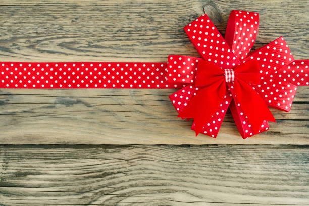 Top view of a gift box with a white ribbon bow on a red polka dot background, evoking celebration and elegance.