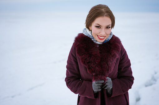 Beautiful woman in a warm coat on a winter background. Young caucasian brunette woman smiling in winter. Beautiful make-up . Happy posing on camera