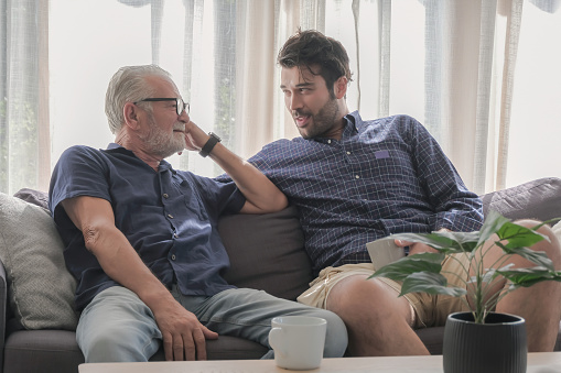 Sharing family story and authentic lifestyle concept. Two of dad and his son are relax talking in happy moment at cozy living room warmth house during holiday with coffee cup on the desk.