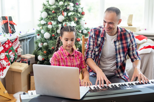 father and daughter at the piano with Christmas decor.