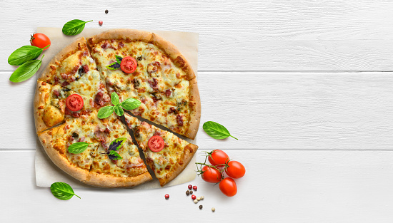 Supreme pizza on white wooden table with tomatoes and basil top view, copy space