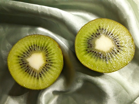 two halves of kiwi fruit, on a green cloth background