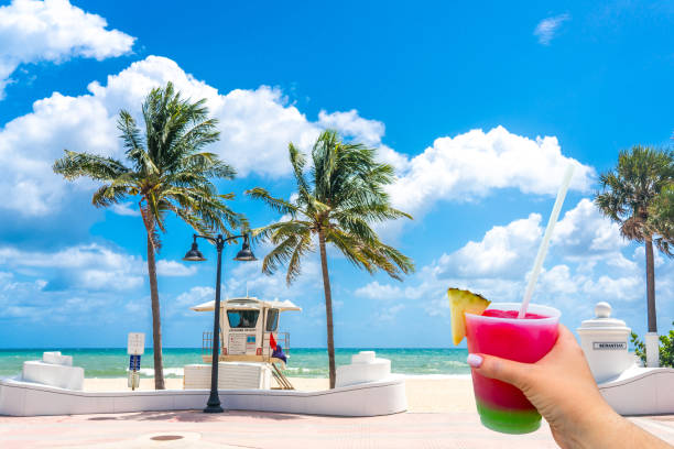 Seafront beach promenade with hand holding cocktail and palm trees on background on sunny day in Fort Lauderdale in Florida USA stock photo
