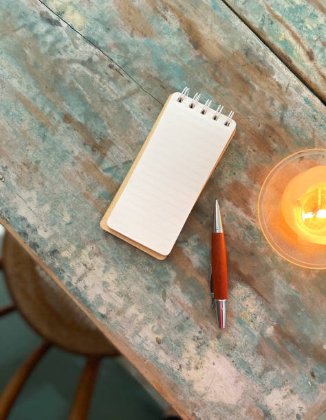istock Weathered wooden desk with a lit candle, notepad and pen 1439448431