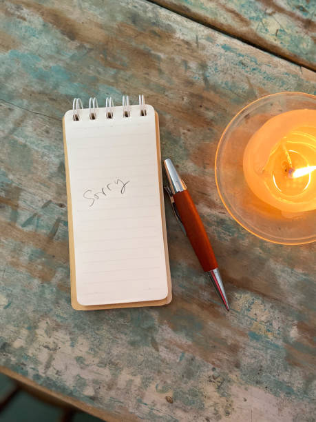 istock Weathered wooden desk with a lit candle, a notepad that says “Sorry’ and pen 1439448562