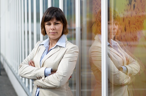 A businesswoman in a suit standing in front of a glass window with crossed arms