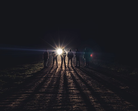 A group of unknown people on the road at night with the right car light in the background - mystery concept