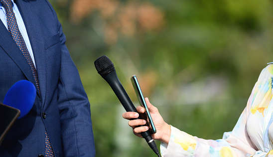 Open-air media interview, female news reporters holding microphones and smart phones