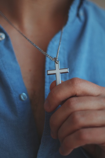 A vertical closeup shot of a male holding a silver necklace with a cross pendant