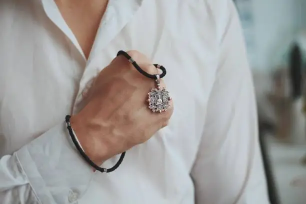 Photo of Closeup shot of a male holding a charm necklace with a silver pendant and a black cord