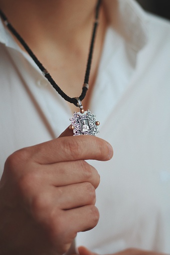 A closeup shot of a male holding a charm necklace with a silver pendant and a black cord