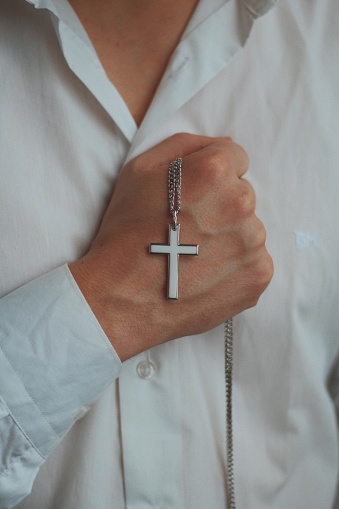 A closeup shot of a religious male holding a silver necklace with a cross pendant