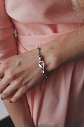 A closeup shot of a female in a pink dress wearing a beautiful silver bracelet with a heart pendant