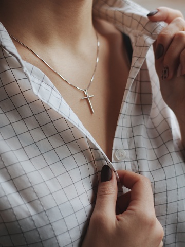 A closeup shot of a female wearing a white shirt and a delicate silver charm necklace