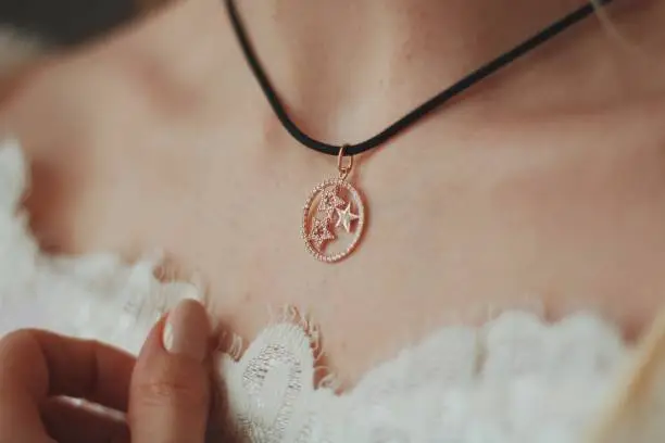 A closeup shot of a bride wearing a pendant necklace with a black cord