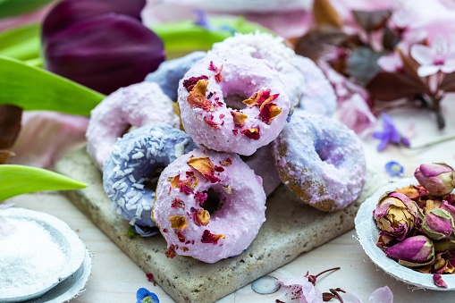 A high angle shot of some blue and purple vegan donuts surrounded by flowers on a table