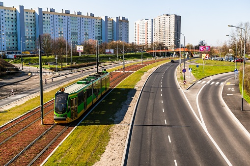 Poznan, Poland – March 24, 2020: Zegrze street with road and green public transport tram on a track. High apartment buildings in the background.