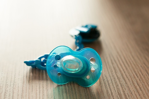 A closeup shot of a blue pacifier on a table with a blurred background