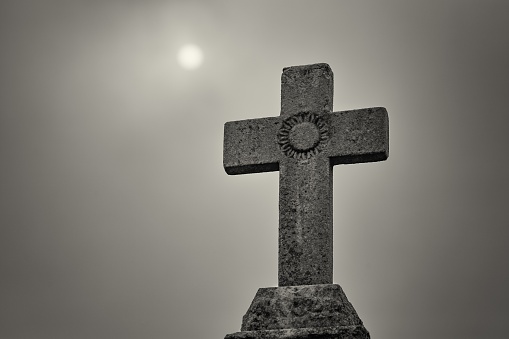 A statue of a stone cross in the graveyard with the sky in the background in New Orleans