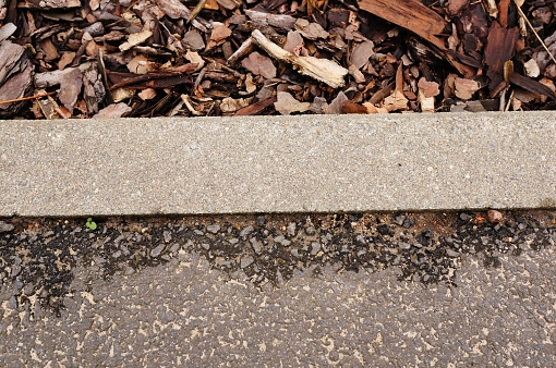A top view shot of the edge of a concrete path with bark chips