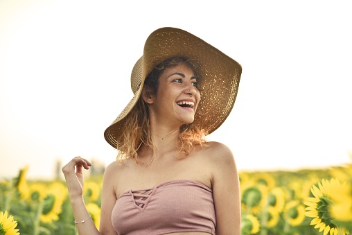 A smiling young woman wearing a hat in the sunflower field - the concept of happiness