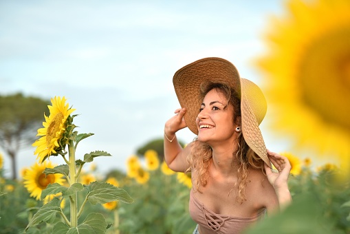 A smiling young woman wearing a hat in the sunflower field - the concept of happiness