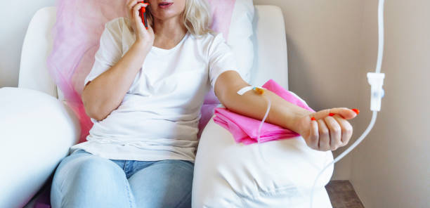 mulher no hospital falando ao telefone celular enquanto a agulha está no braço, terapia de vitamina iv infusão de gotejamento no sangue das mulheres - blood cell fotos - fotografias e filmes do acervo