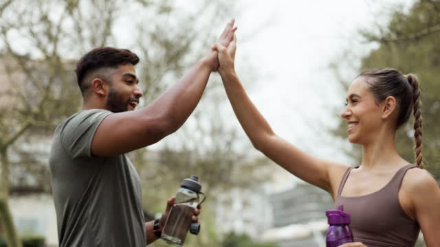Water, couple and high five for success, exercise and support for fitness goal. Workout trainer and client woman with celebration, achievement and hydrate after training in the city or New york