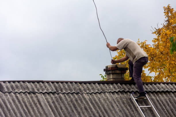 uno spazzacamino pulisce il camino dalla fuliggine sul tetto di una casa di paese contro un cielo grigio con uno spazio per le copie, preparandosi per la stagione di riscaldamento - chimney sweeping foto e immagini stock