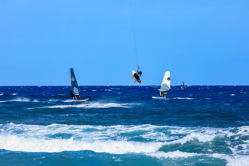 Ein Kitesurfer beim springen und zwei Windsurfer beim Strand \