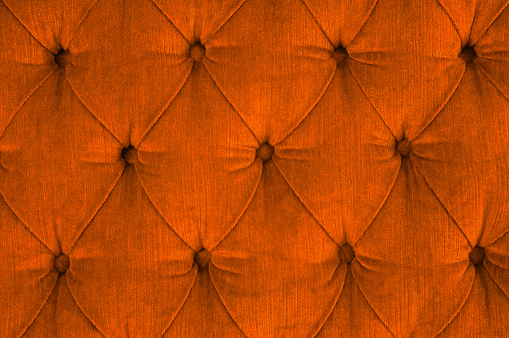 Close-up of a orange quilted velvet sofa with upholstered buttons (diamond stitching) / Rautenheftung