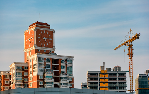 A clock tower at the top of a residential area and a tower crane on a nearby construction site in Shanghai, China.