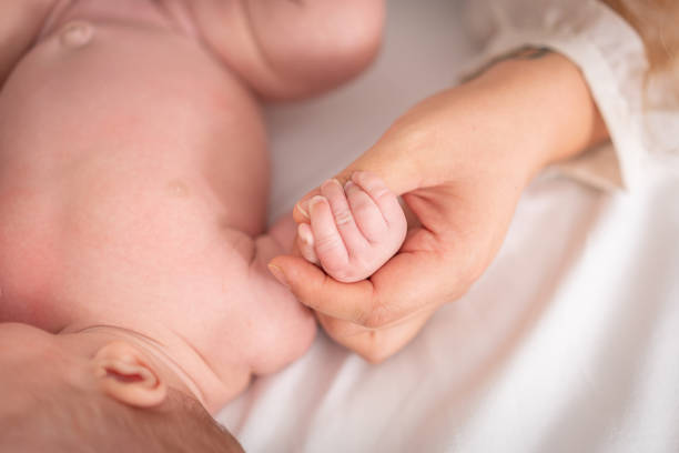istock Baby hand holding finger mom on bed with white background 1439484239