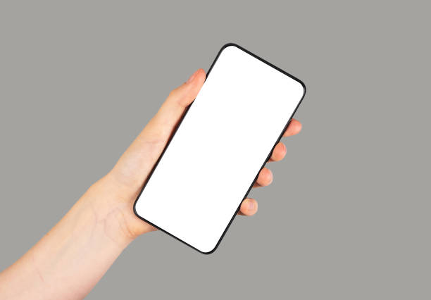 istock Hand holding phone mockup in angled position on grey background. Smartphone template with empty screen for mobile application, social media site advertisement. 1439487759