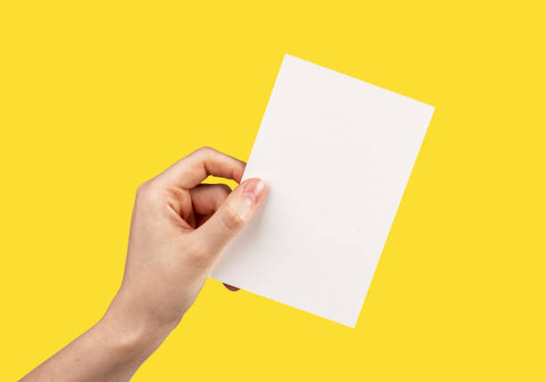 istock Hand holding greeting card mockup on yellow background. White empty paper for text. Invitation, letter, gift, certificate template 1439487760