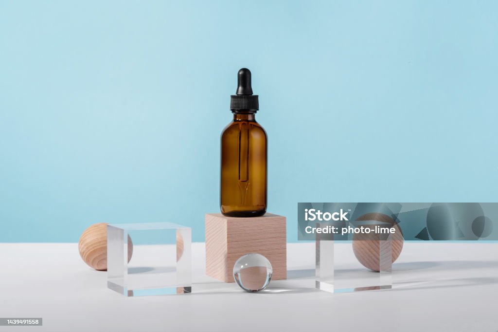 Oil cosmetics amber product packaging with stylish props. Serum cosmetic bottle with peptides and retinol on acrylic and wooden blocks on blue background. Serum dropper mockup on pedestal podium Acid Stock Photo
