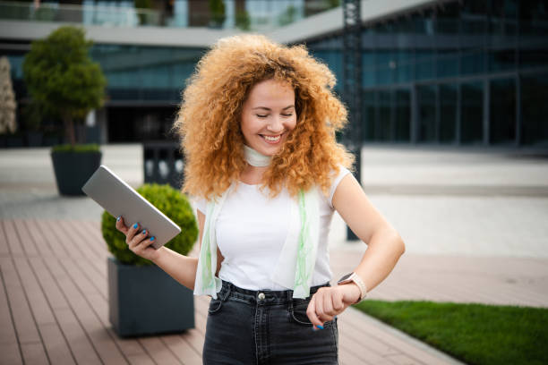 Portrait of a beautiful redhead young woman checking the time and using tablet while walking