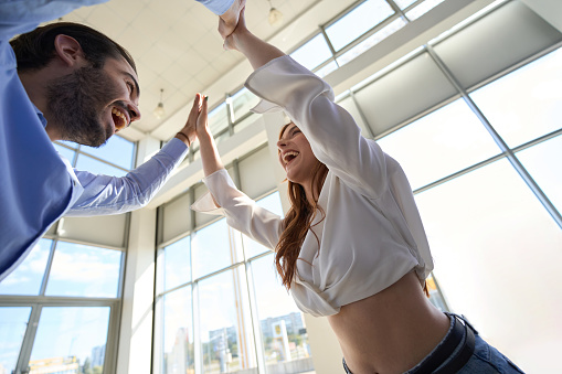 Low angle of joyous male giving high five to his merry female companion in showroom