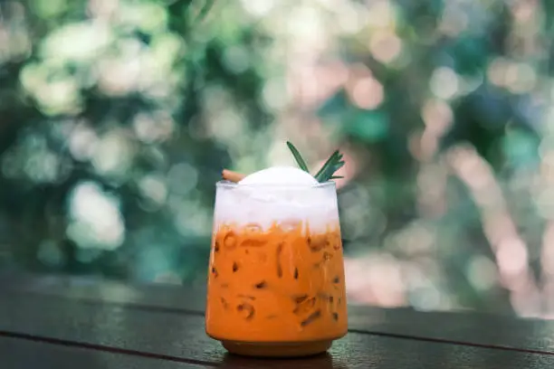 Photo of Thai Milk Tea, Milk ice tea, Cheddar is a traditional Thai drink that has long been popular, fresh and sweet dessert on a wooden saucer, vintage wooden table in cafe.