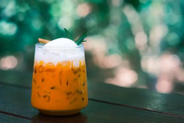 Photo of Thai Milk Tea, Milk ice tea, Cheddar is a traditional Thai drink that has long been popular, fresh and sweet dessert on a wooden saucer, vintage wooden table in cafe.