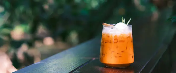 Photo of Thai Milk Tea, Milk ice tea, Cheddar is a traditional Thai drink that has long been popular, fresh and sweet dessert on a wooden saucer, vintage wooden table in cafe.