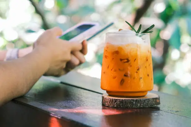 Photo of Thai Milk Tea, Milk ice tea, Cheddar is a traditional Thai drink that has long been popular, fresh and sweet dessert on a wooden saucer, vintage wooden table in cafe.