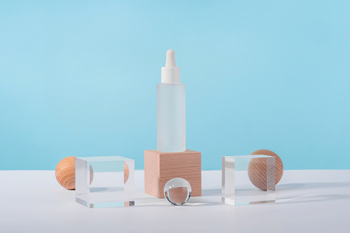 Oil cosmetics transparent product packaging with stylish props. Serum cosmetic bottle with peptides and retinol on acrylic and wooden blocks on blue background. Serum dropper mockup on pedestal podium