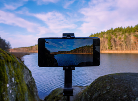 Close-up of mobile phone on a tripod by lake against sky