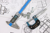 micrometer, caliper and hardware on a background of engineering drawings. Science, mechanics and mechanical engineering.