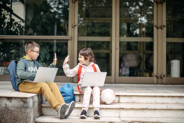 explain lesson boy showing girl on computer helping study friends older brother younger sister online learning spending time together sitting by window with a laptop in hands teenagers 14 15 years old