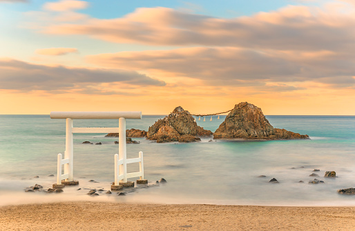 Long exposure seascape photography of the Itoshima Beach and its famous  Sakurai Futamigaura's Meoto Iwa Couple Rocks protected by a sacred white Shinto torii gate in the evening sunset light.